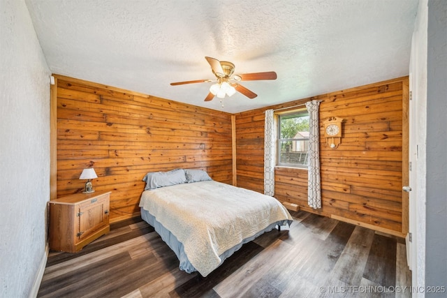 bedroom featuring ceiling fan, wood walls, baseboards, a textured ceiling, and wood finished floors