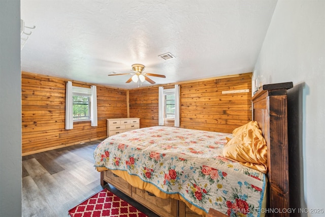 bedroom with wood finished floors, wood walls, ceiling fan, visible vents, and a textured ceiling