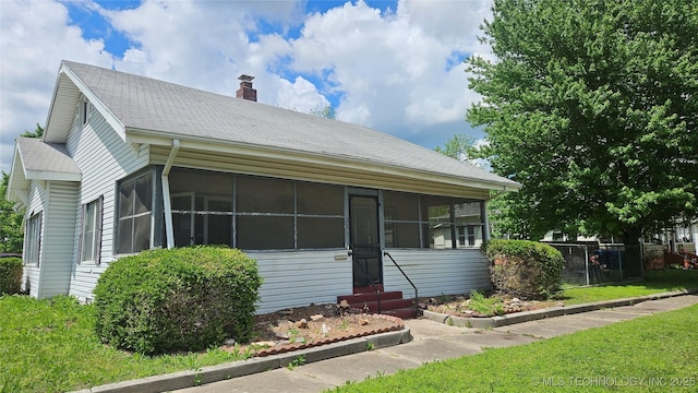 bungalow-style house with a sunroom, a front lawn, a chimney, entry steps, and fence