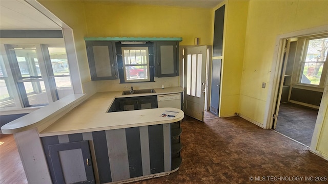 kitchen with white dishwasher, a peninsula, light countertops, and a sink