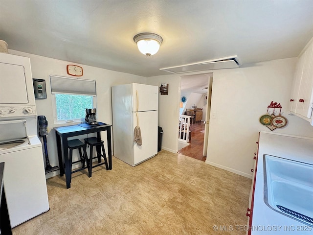 kitchen with light floors, freestanding refrigerator, a sink, baseboards, and stacked washing maching and dryer