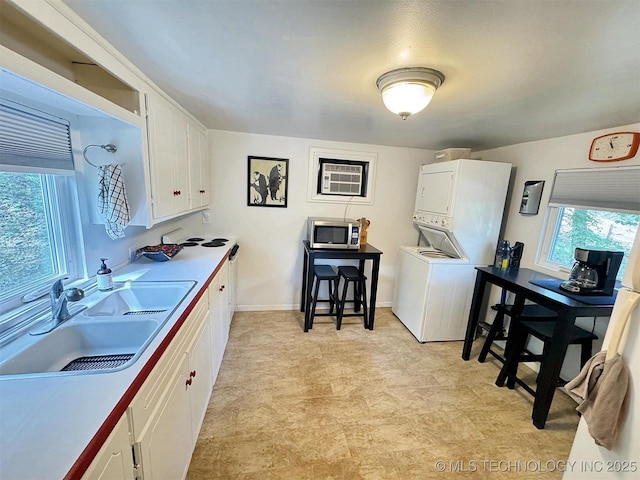 laundry area featuring stacked washer / dryer, a sink, baseboards, light floors, and laundry area