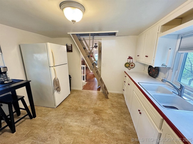 kitchen featuring light floors, freestanding refrigerator, light countertops, white cabinets, and a sink