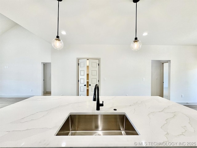 kitchen featuring light stone counters, a sink, and decorative light fixtures