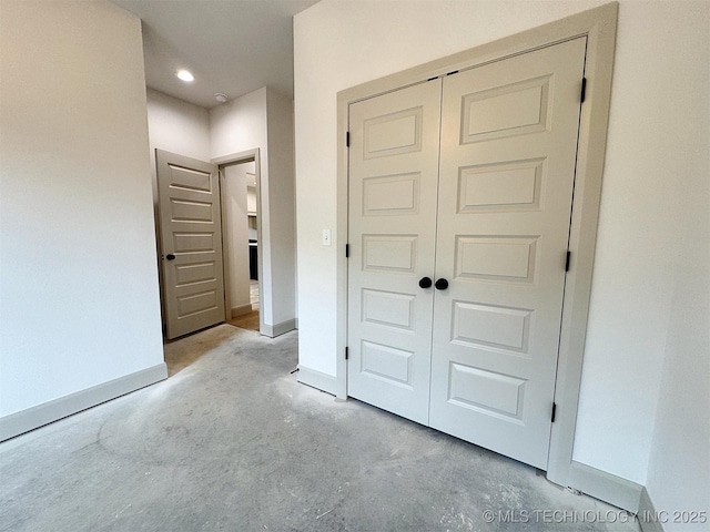 unfurnished bedroom with baseboards, unfinished concrete flooring, and a closet