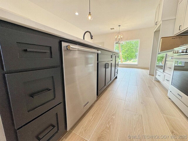 kitchen with hanging light fixtures, a notable chandelier, appliances with stainless steel finishes, light wood-style flooring, and white cabinetry