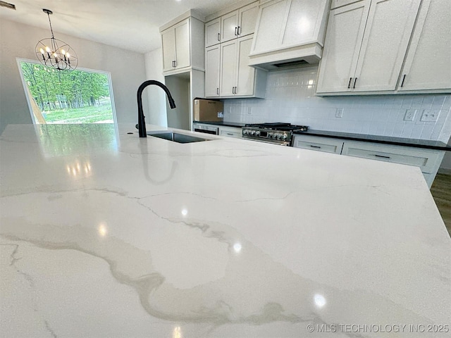 kitchen with decorative backsplash, premium range hood, high end stove, a sink, and a notable chandelier