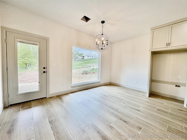 unfurnished dining area featuring baseboards, light wood-type flooring, and a chandelier