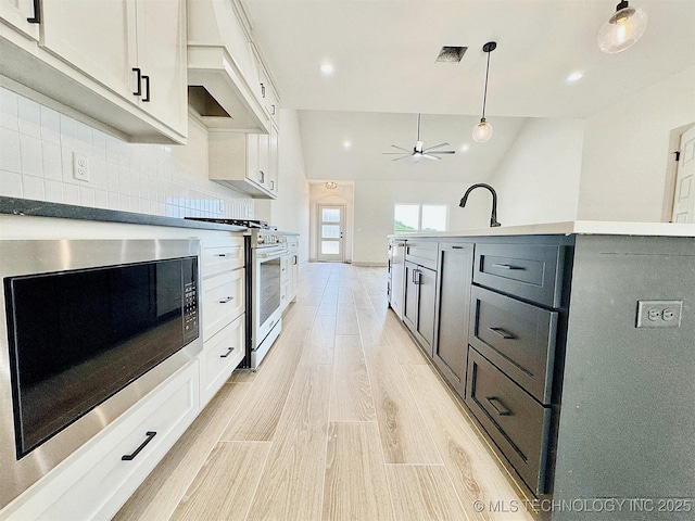 kitchen featuring stainless steel appliances, light wood-type flooring, custom range hood, tasteful backsplash, and pendant lighting