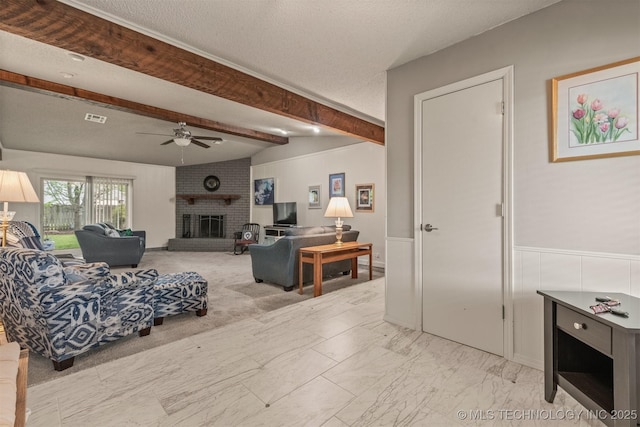 living room featuring a brick fireplace, ceiling fan, vaulted ceiling with beams, visible vents, and wainscoting