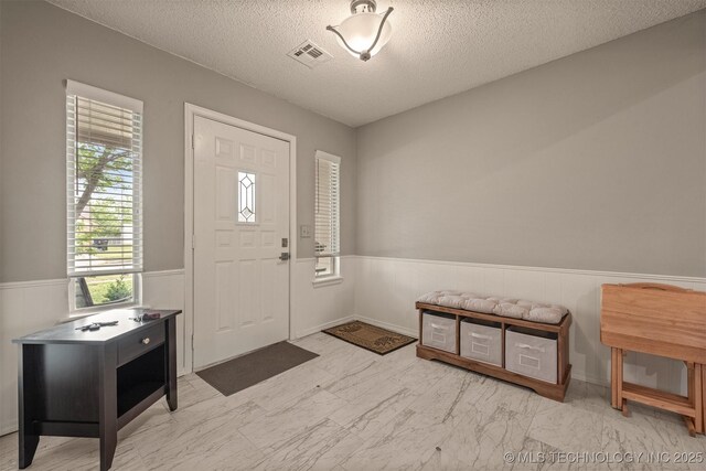 entryway featuring visible vents, a wainscoted wall, a textured ceiling, and marble finish floor
