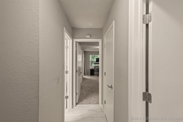 hall with a textured ceiling, a textured wall, and marble finish floor