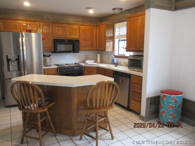 61 Cedar, Ardmore, OK 73401 - kitchen featuring light tile patterned floors, black appliances, a kitchen bar, and light countertops
