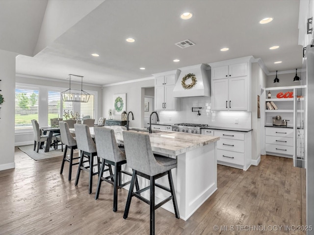13651 S 26th St, Jenks, OK 74008 - kitchen with custom range hood, ornamental molding, white cabinets, backsplash, and a kitchen island with sink