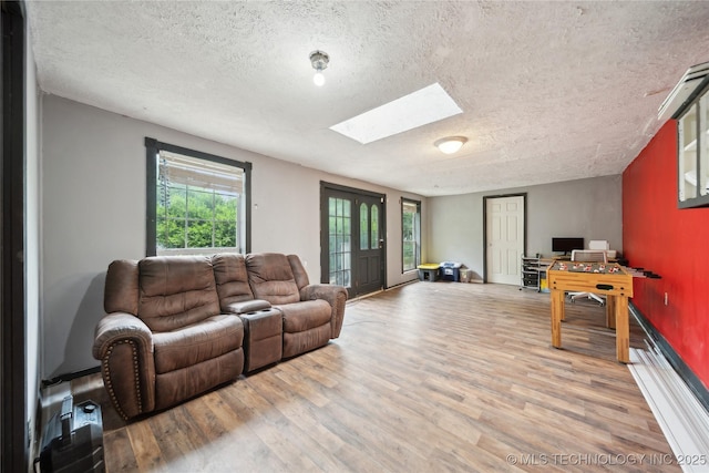 living area with light wood-style floors, a skylight, and a textured ceiling