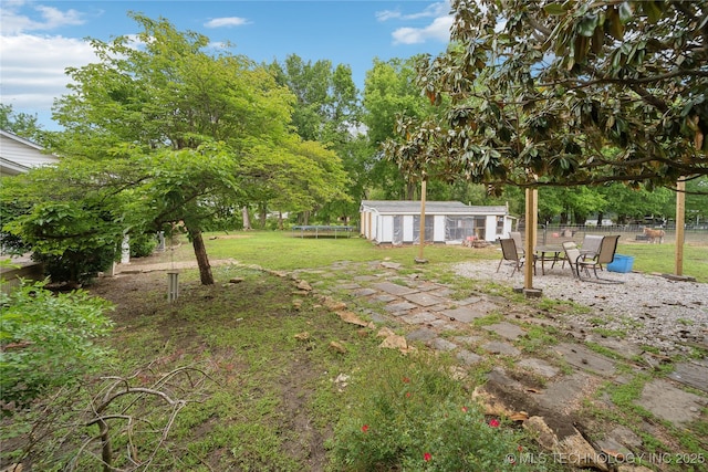 view of yard featuring a trampoline, fence, an outdoor structure, and a patio area