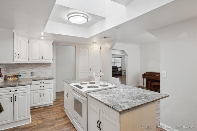 kitchen featuring tasteful backsplash, wood finished floors, arched walkways, white cabinetry, and white electric range oven