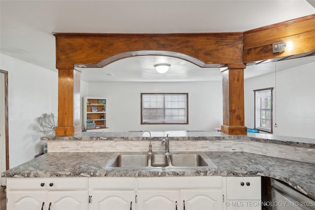 kitchen featuring white cabinetry, decorative columns, stainless steel dishwasher, and a sink