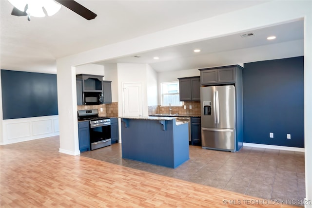 kitchen with ceiling fan, a breakfast bar, stainless steel appliances, a kitchen island, and visible vents