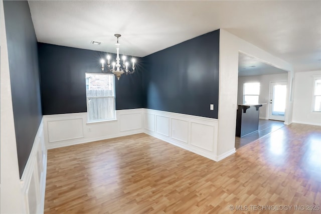 unfurnished room with visible vents, a notable chandelier, a wealth of natural light, and light wood-type flooring