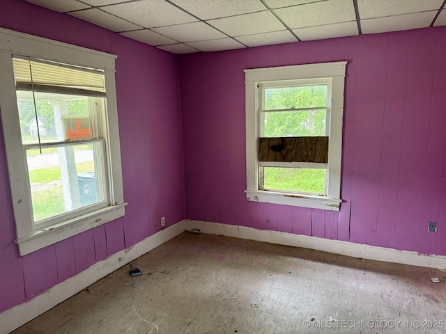 empty room with baseboards, a drop ceiling, and plenty of natural light