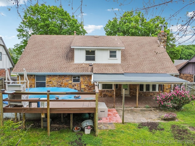 rear view of property featuring a deck, a patio area, a shingled roof, and stone siding
