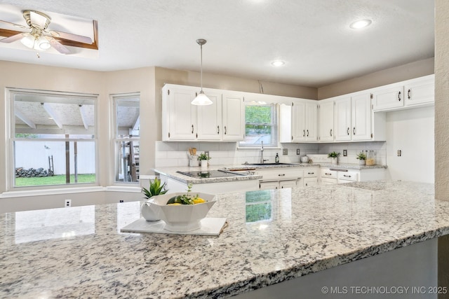 kitchen featuring light stone counters, white cabinetry, hanging light fixtures, and a sink