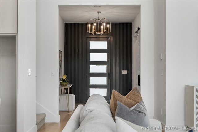 entrance foyer featuring a barn door, light wood-type flooring, a notable chandelier, and baseboards