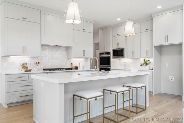 kitchen with recessed lighting, stainless steel appliances, light countertops, light wood finished floors, and a sink
