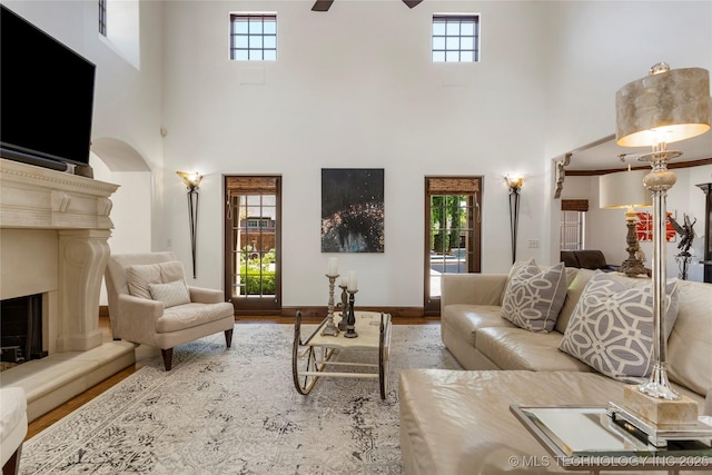 living area featuring a fireplace with raised hearth, a towering ceiling, ceiling fan, and arched walkways
