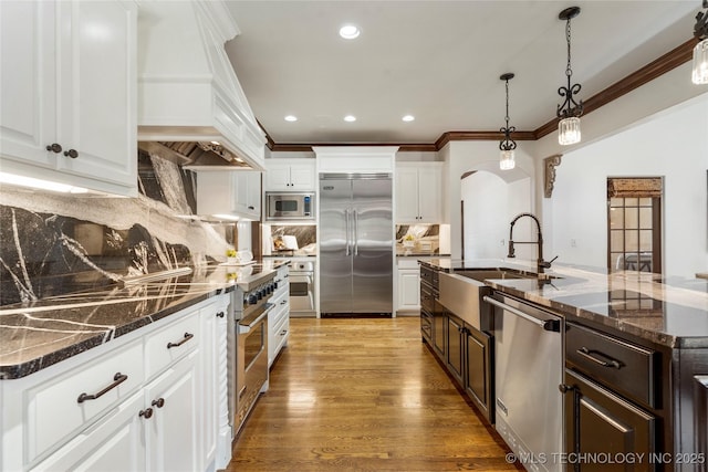 kitchen with crown molding, built in appliances, dark brown cabinets, arched walkways, and a sink