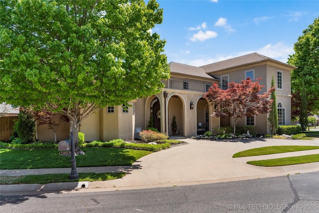 mediterranean / spanish home with a front lawn, stucco siding, a balcony, curved driveway, and covered porch