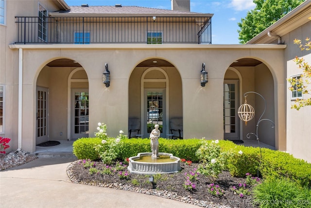 property entrance featuring stucco siding, a balcony, and a chimney