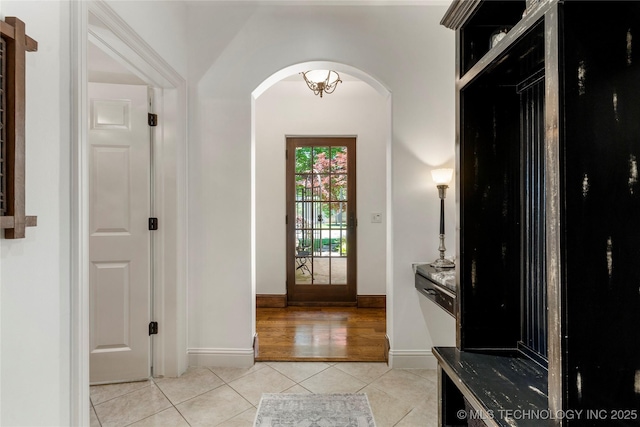 interior space featuring light tile patterned floors, arched walkways, and baseboards