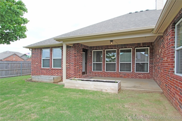rear view of property featuring brick siding, a yard, roof with shingles, a vegetable garden, and fence
