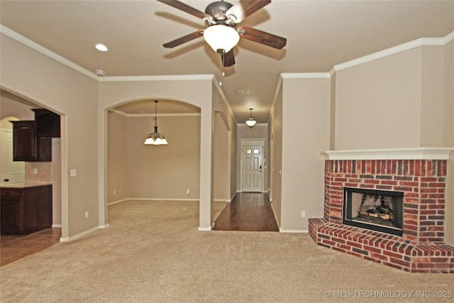 unfurnished living room with arched walkways, carpet, ceiling fan with notable chandelier, a fireplace, and crown molding