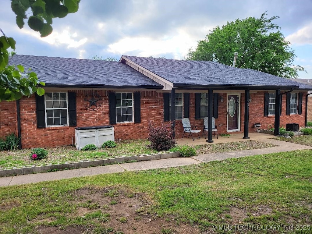 ranch-style home featuring a front lawn, a porch, a shingled roof, and brick siding
