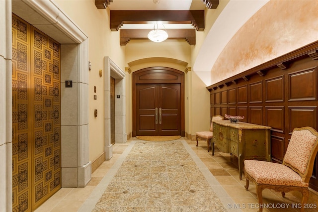 interior space with a towering ceiling, beamed ceiling, elevator, arched walkways, and light tile patterned floors