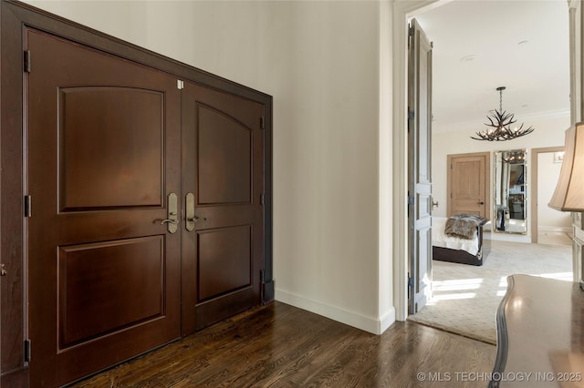 entrance foyer with a notable chandelier, baseboards, dark wood finished floors, and ornamental molding