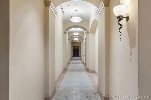 corridor with baseboards, arched walkways, and ornate columns