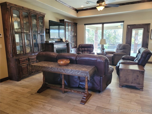 living room featuring crown molding, a ceiling fan, visible vents, and light wood-type flooring