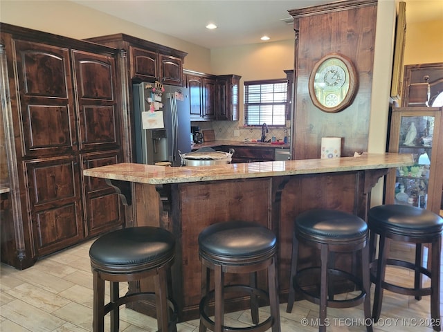 2267 Krebs Lk, Mcalester, OK 74501 - kitchen with stainless steel refrigerator with ice dispenser, light stone counters, a sink, a breakfast bar, and decorative backsplash