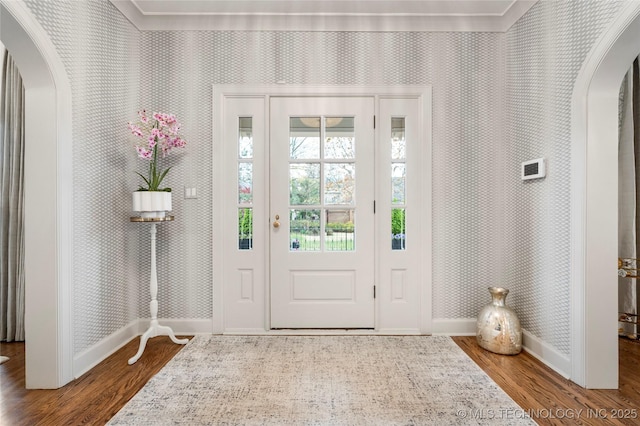 foyer with baseboards, arched walkways, and wood finished floors