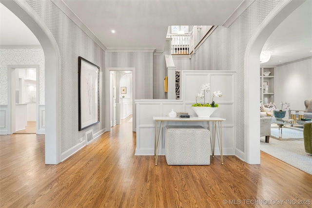 hall featuring visible vents, arched walkways, wood finished floors, ornamental molding, and wallpapered walls