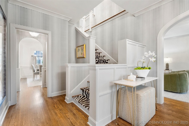hallway featuring arched walkways, wallpapered walls, and wood finished floors