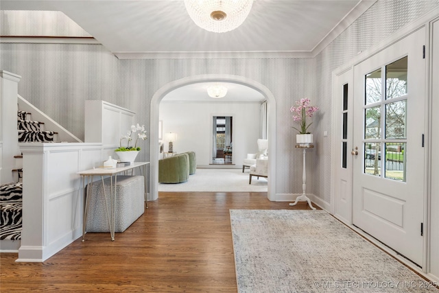 entrance foyer featuring baseboards, arched walkways, wood finished floors, and wallpapered walls