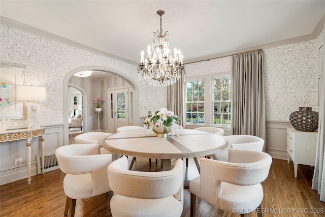 dining area with arched walkways, wainscoting, wood finished floors, and wallpapered walls
