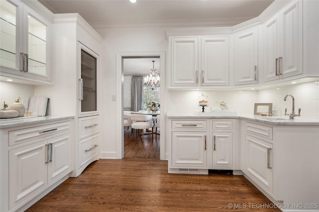 kitchen featuring backsplash, a sink, white cabinets, a notable chandelier, and glass insert cabinets