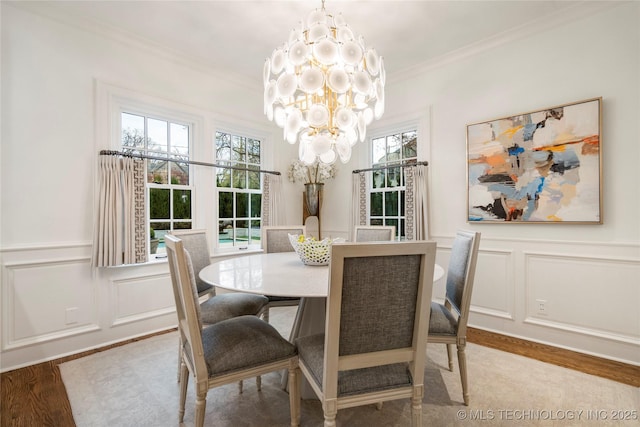 dining room with an inviting chandelier, ornamental molding, a decorative wall, and wood finished floors