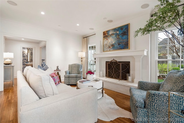 living area featuring recessed lighting, ornamental molding, wood finished floors, and a high end fireplace
